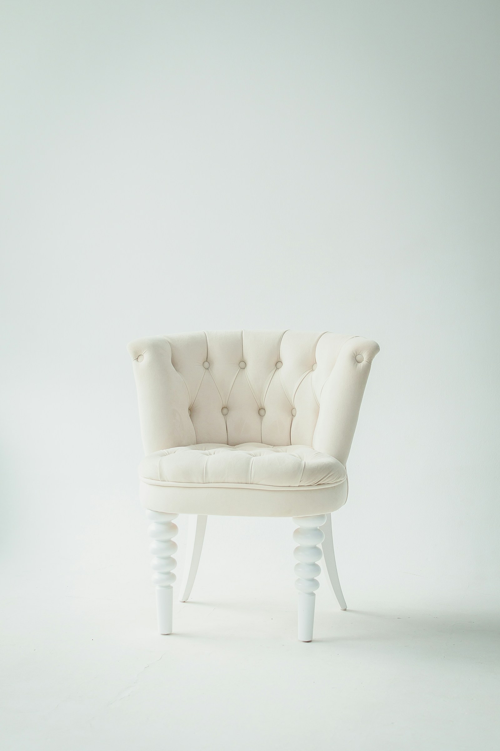 A cream button-backed upholstered chair with turned wooden legs